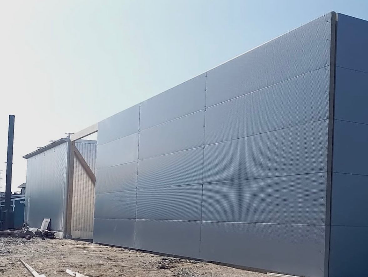 Suuri, aaltoileva metallirakennus aurinkoisessa ympäristössä, jossa on sininen taivas.