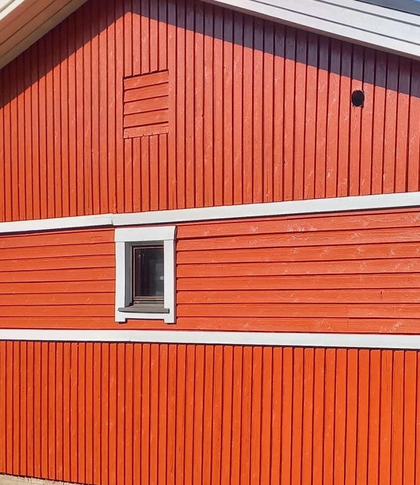 Punainen puutalo, jossa on valkoiset reunukset, pieni ikkuna ja tuuletusaukko.