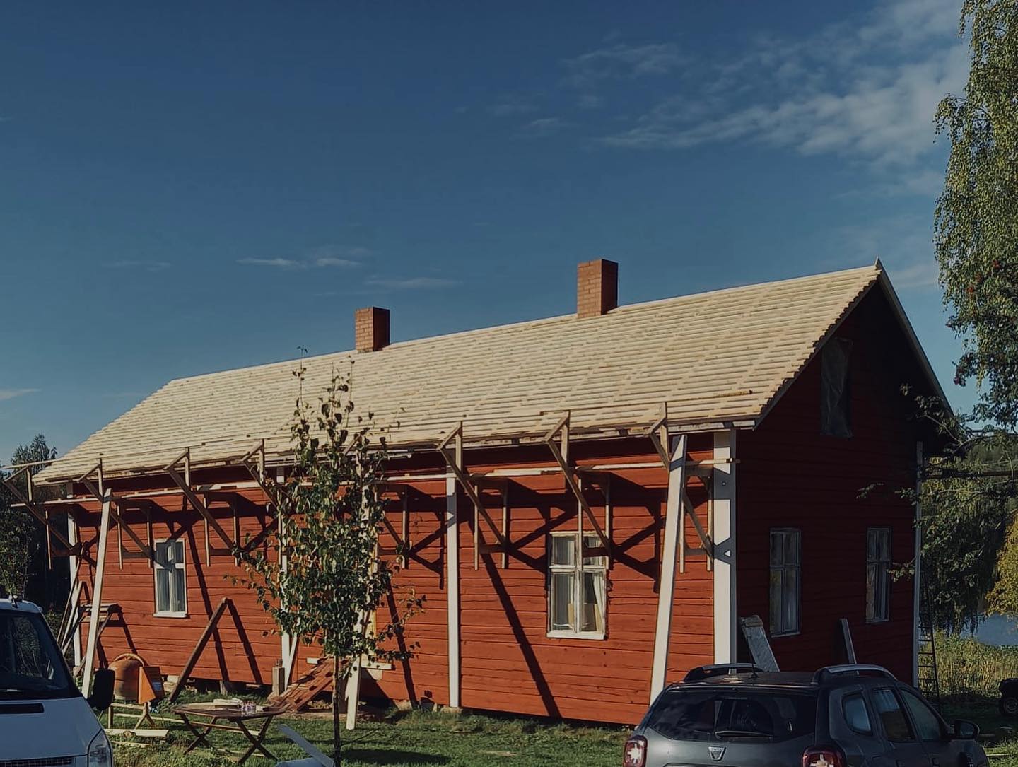 Punainen puutalo, jossa on uusi vaalea katto ja valkoiset tukipuut, aurinkoisessa säässä.