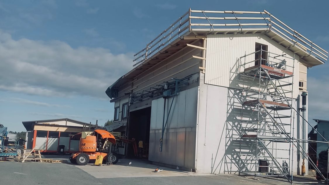 Rakennustyömaa, jossa on valkoinen rakennus, oranssi nosturi ja metallinen rakennusteline aurinkoisessa säässä.