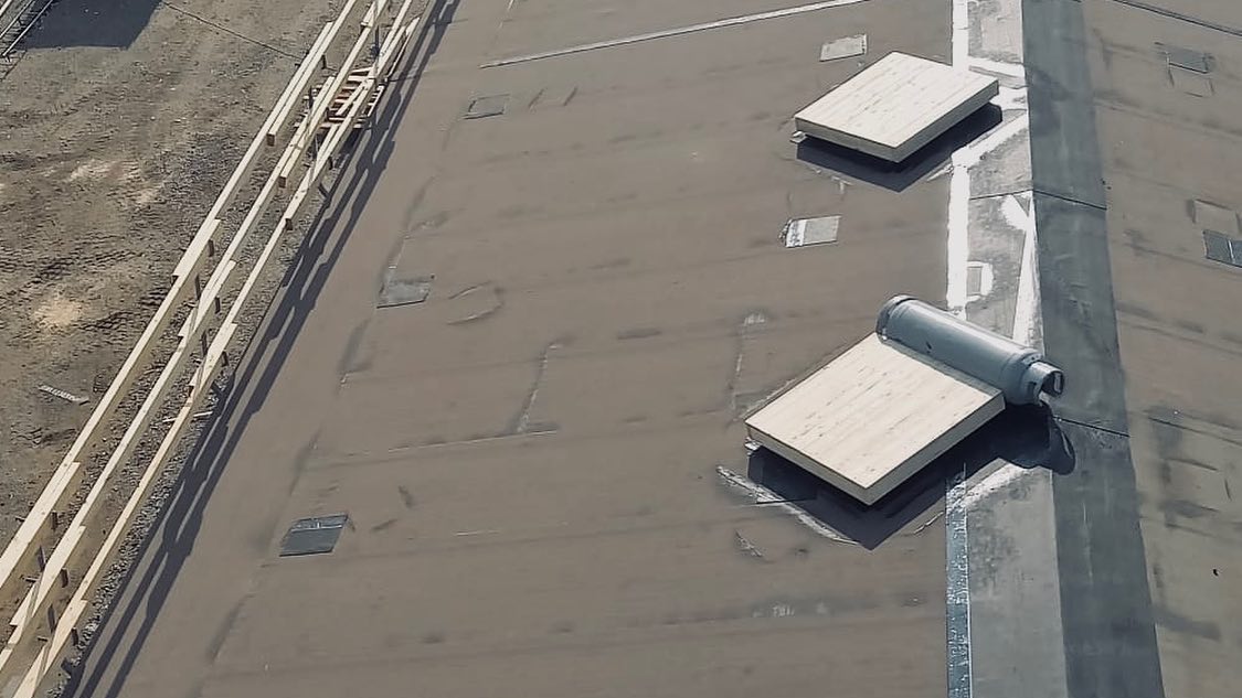 Ylänäkymä tasakatosta, jossa on puutavaraa, kaksi puista koroketta ja harmaa sylinteri. Valo on kirkas.